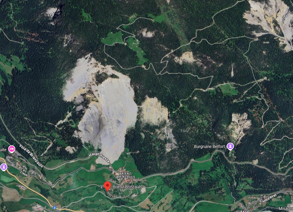 Aerial view of the Brienz region in the canton of Graubünden, showing green landscape, forests and possible waterlogged areas. A landslide is visible in the upper section.