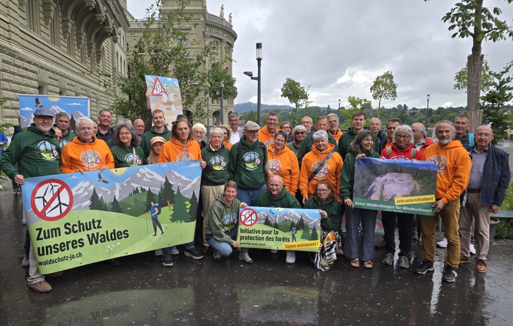 Gruppe von Menschen mit T-Shirts und Bannern für den Waldschutz, versammelt vor einem Regierungsgebäude in der Schweiz.