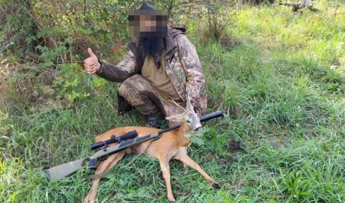 Bündner Hobby-Jäger hebt den Daumen neben einem erschossenen Reh, auf dem sein Gewehr liegt, Gesicht unkenntlich gemacht